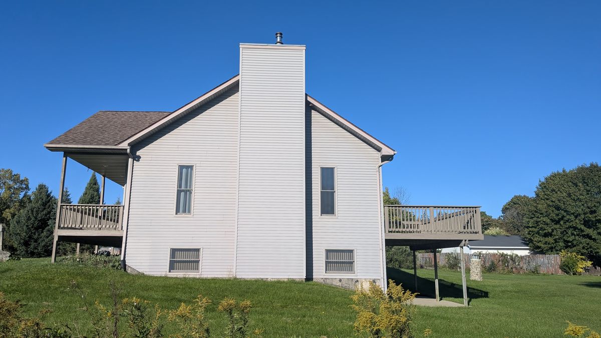 Side of the house with the chimney running up the outside wall between the porch and the deck